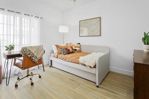 A white couch with a blanket on it sits in a room with a wooden floor and a chair with wheels.