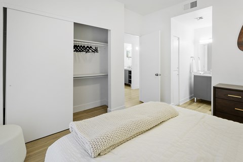 A white bed with a white pillow is in the foreground of a room with a white wardrobe and a white door.