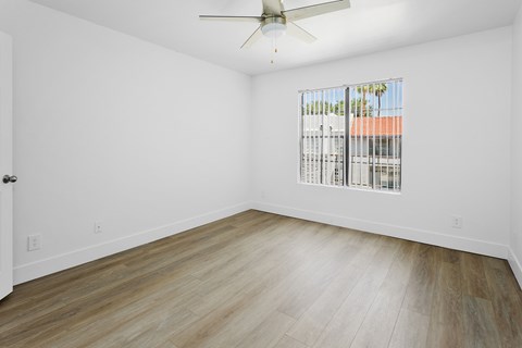 A room with a ceiling fan and a window showing a view of a building.
