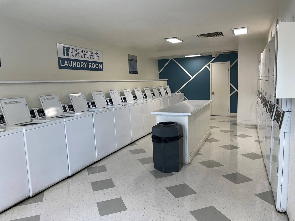 a row of laundry machines in a room with a trash can