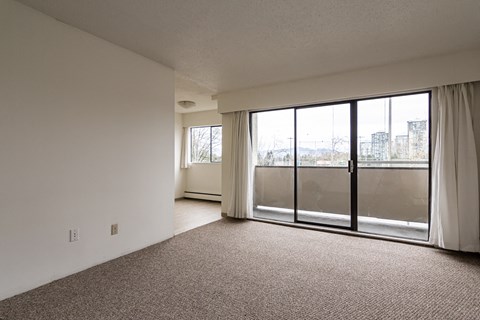 A room with a carpeted floor and a large window with a view of buildings outside.