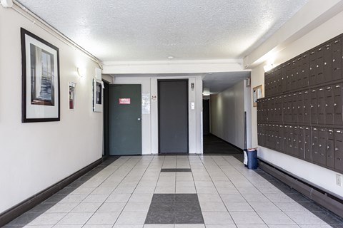 A hallway with a black and white tiled floor, a door with a red sign above it, and a wall with a framed picture on it.