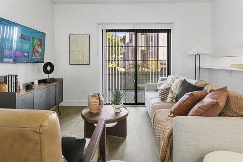 A living room with a tan couch, a brown leather chair, a wooden coffee table, and a white wall with a framed map.