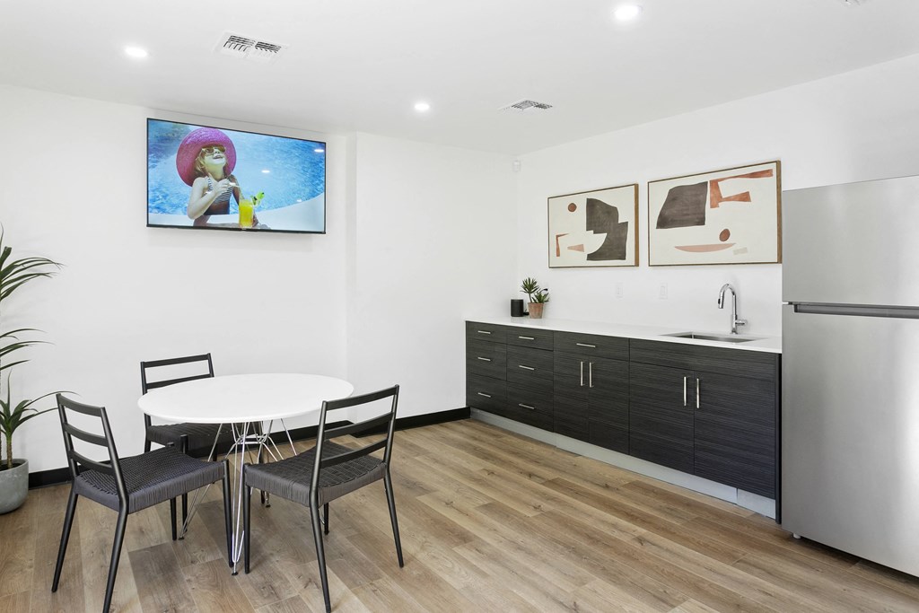 a dining area with a small table and chairs and a kitchenette with a refrigerator and sink