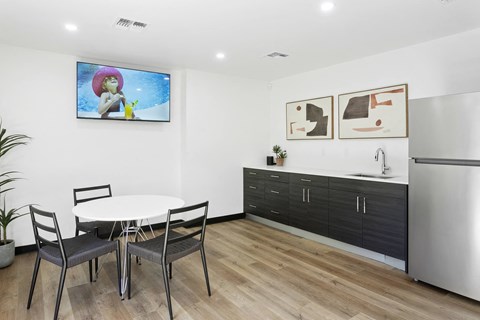 a dining area with a small table and chairs and a kitchenette with a refrigerator and sink