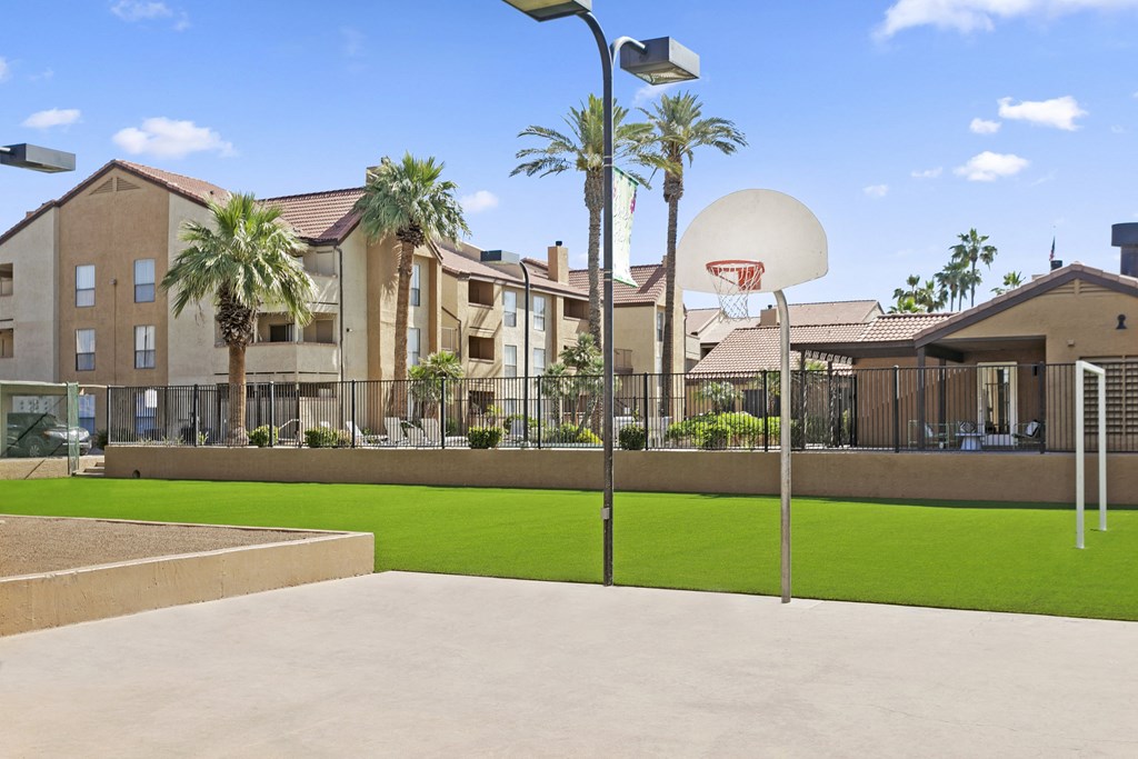 a basketball hoop sits in the middle of a grassy area with apartment buildings in the background