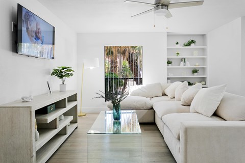 A living room with a white couch and a television mounted on the wall.