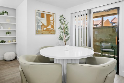A white table with two chairs in front of a framed picture and a potted plant.