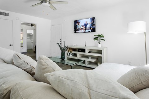 A living room with a white couch and a flat screen TV mounted on the wall.