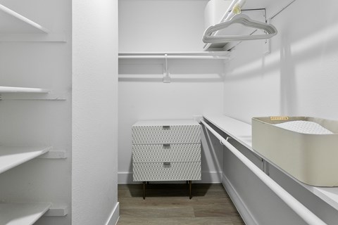 A walk-in closet with white shelves and a white dresser.