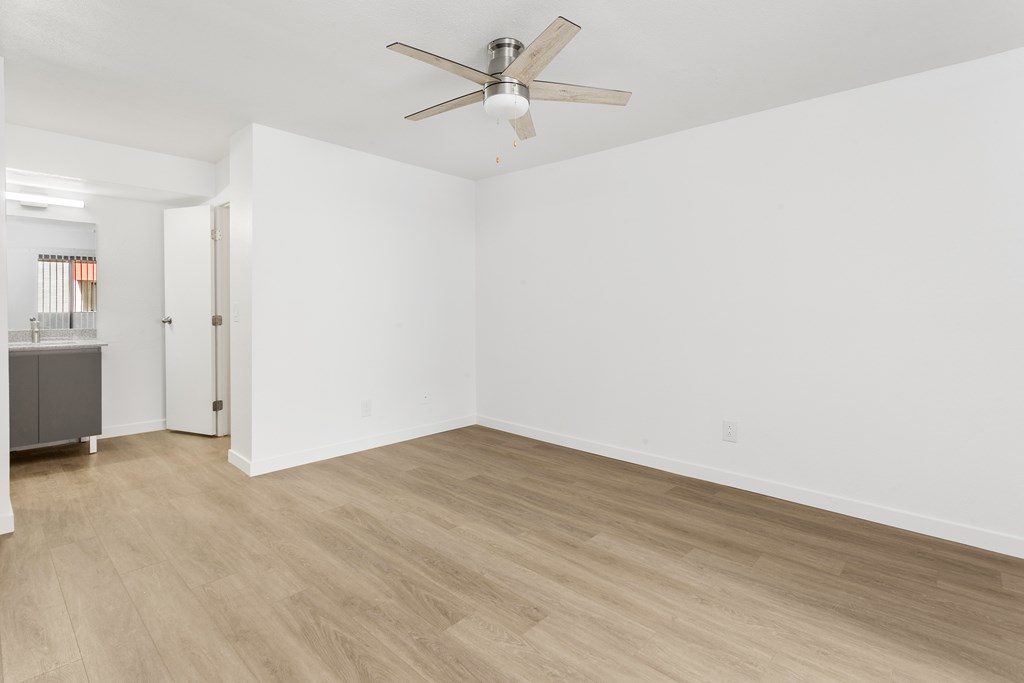 A room with a ceiling fan and light, hardwood floors, and white walls.