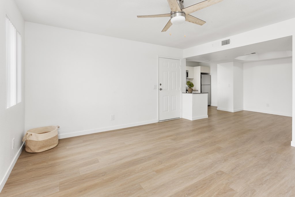 A room with a ceiling fan and light, hardwood floors, and a white door.