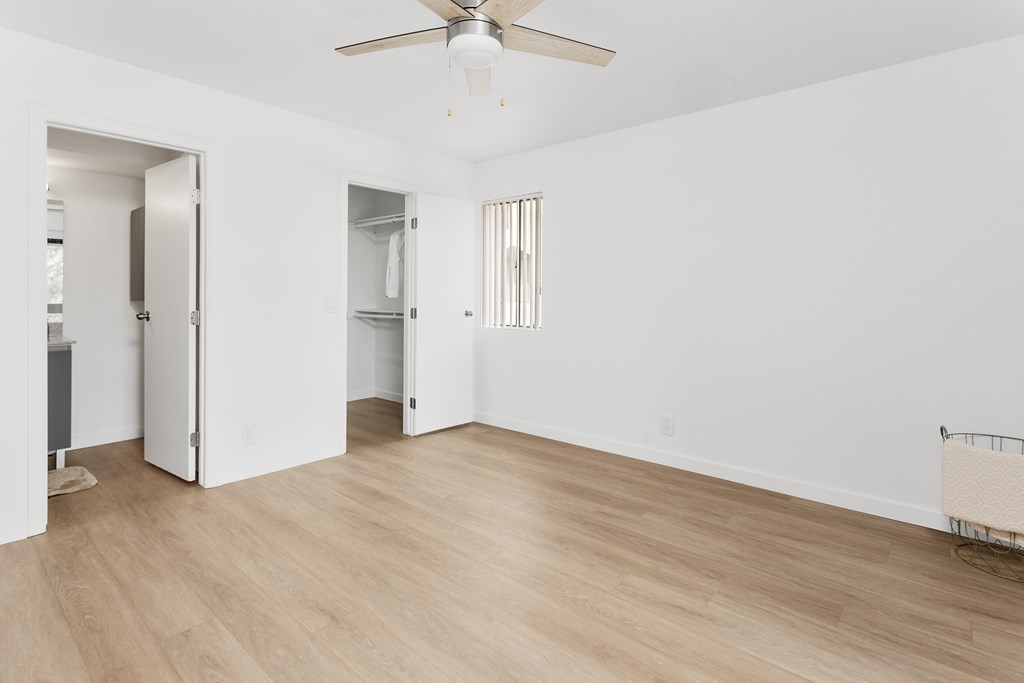 A room with a ceiling fan and light fixture, two open doors, and a chair.