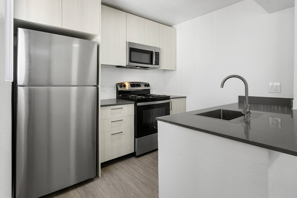 A modern kitchen with a stainless steel refrigerator and black countertops.