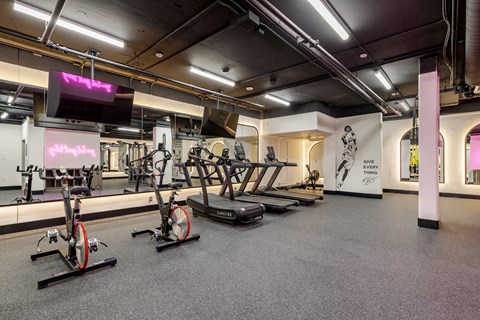 A gym with a row of stationary bikes and a television.