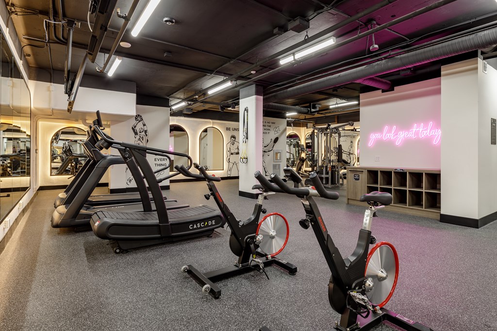 A gym with a row of stationary bikes and a neon sign that says
