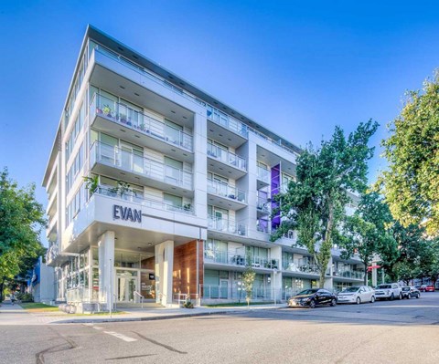 The image shows a modern apartment building named EVAN with cars parked in front and trees beside it.