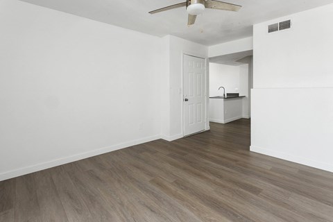 A room with a white ceiling and a fan, and a kitchen area with a stove and a refrigerator.