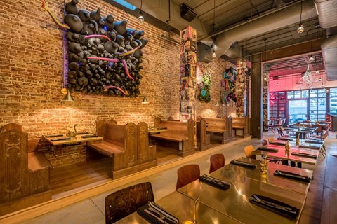 A restaurant with a long table and chairs with a wall hanging on the left.
