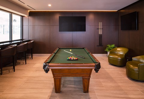 A pool table in a room with leather chairs and a television mounted on the wall.