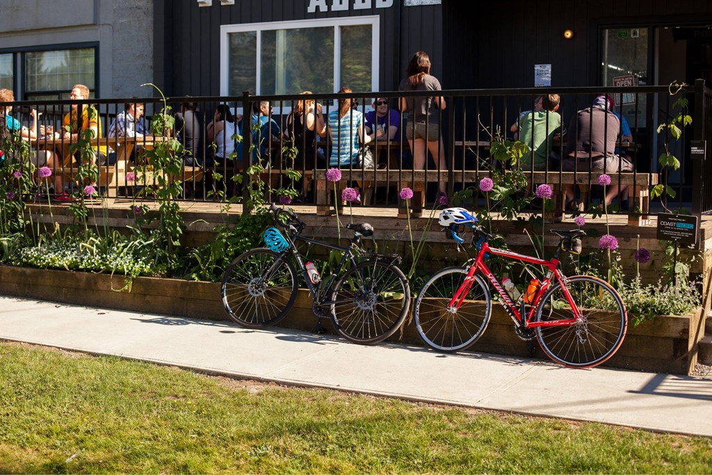 Two bikes are parked on a sidewalk next to a flower bed.