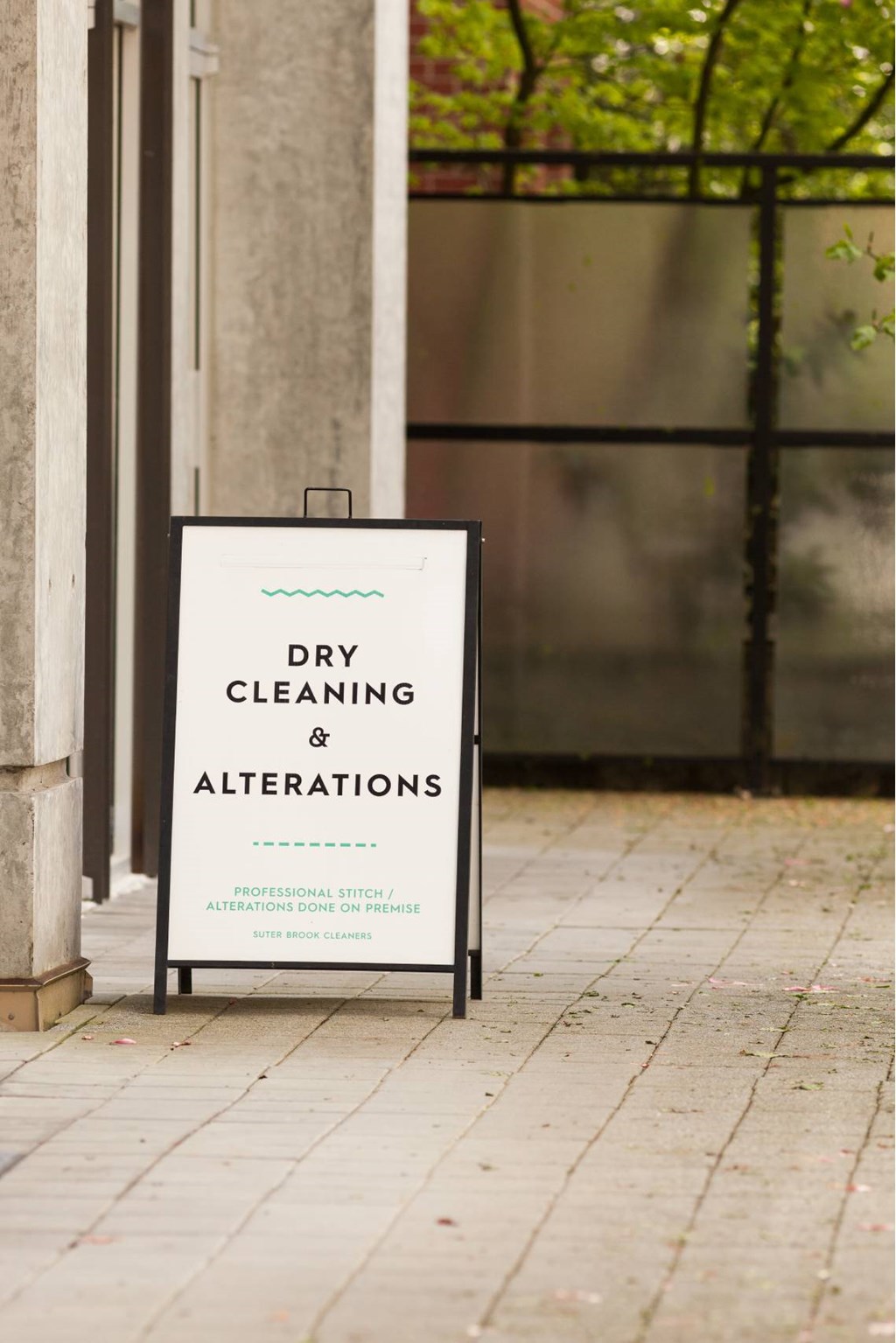 A sign that says dry cleaning and alterations is propped up against a wall.