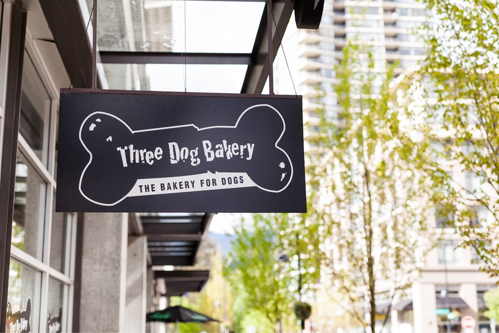 A black and white sign for Three Dog Bakery hangs from a building.