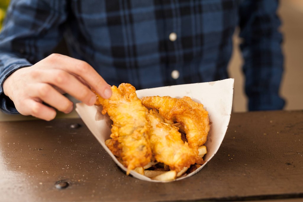 A person in a plaid shirt is holding a paper cone filled with fried food.