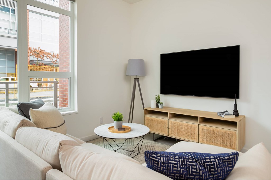 A living room with a white couch, a black screen, and a small table with a plant on it.