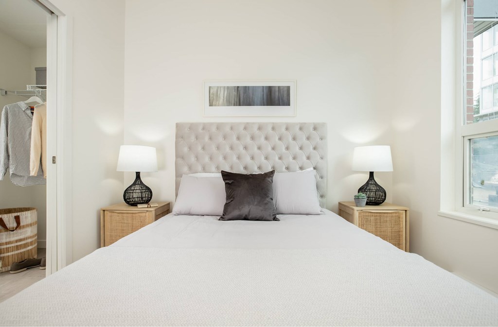 A bed with a white headboard and two pillows sits in a room with two lamps on either side.