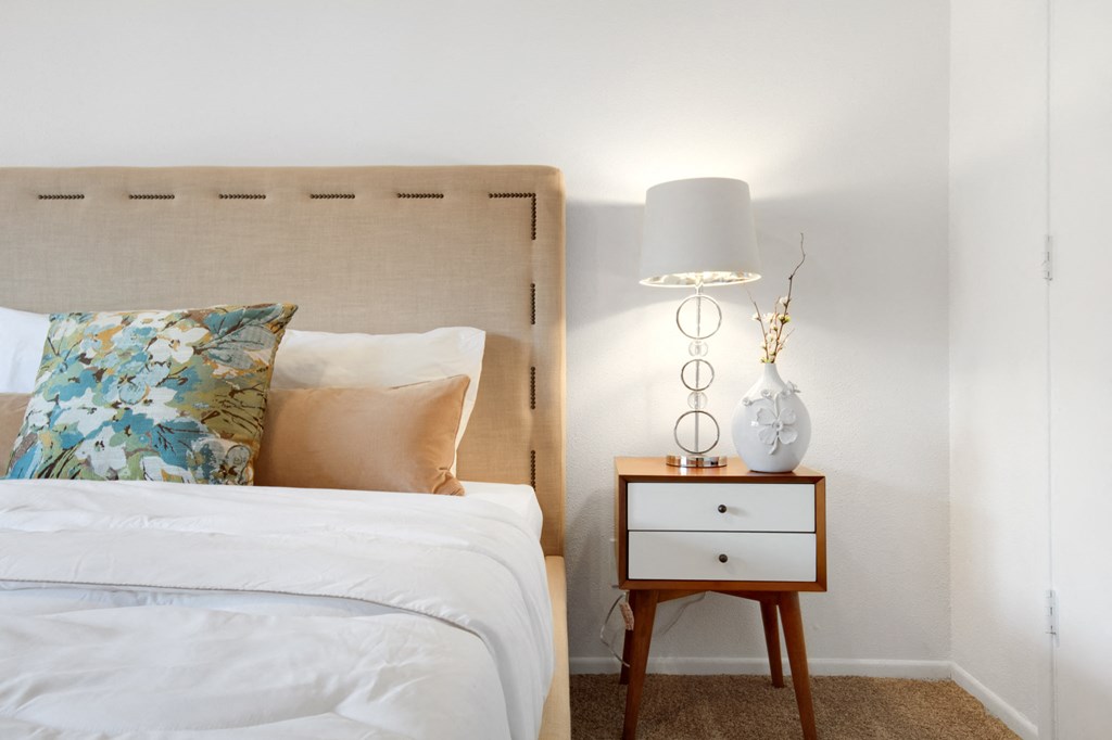 a bedroom with a bed and a nightstand with a lamp and pillows