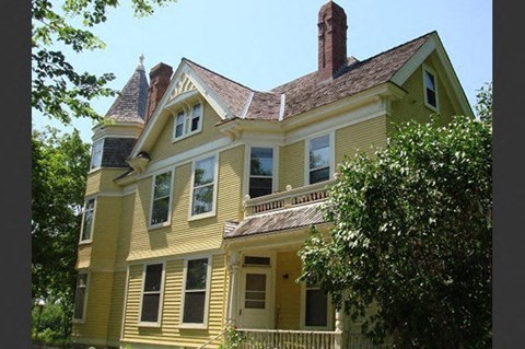 A yellow house with a brown roof and a white door.