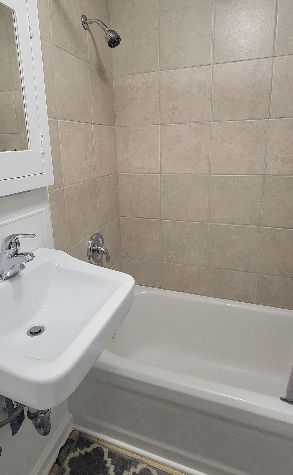 A white sink is mounted on a wall next to a bathtub.