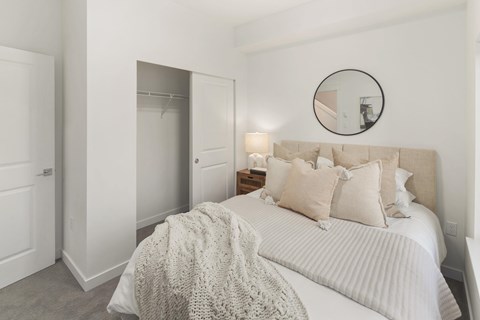 A bedroom with a bed, pillows, and a round mirror on the wall at The Narrows at Clare Apartments , Bremerton, 98310