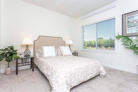 A bedroom with a large bed and a window with blinds.