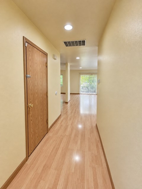 A long hallway with a wooden floor and a door on the left.