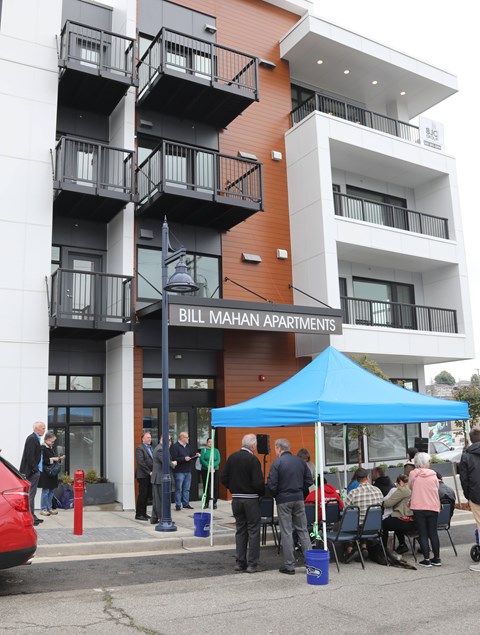 A group of people are standing outside of Bill Mahan Apartments.