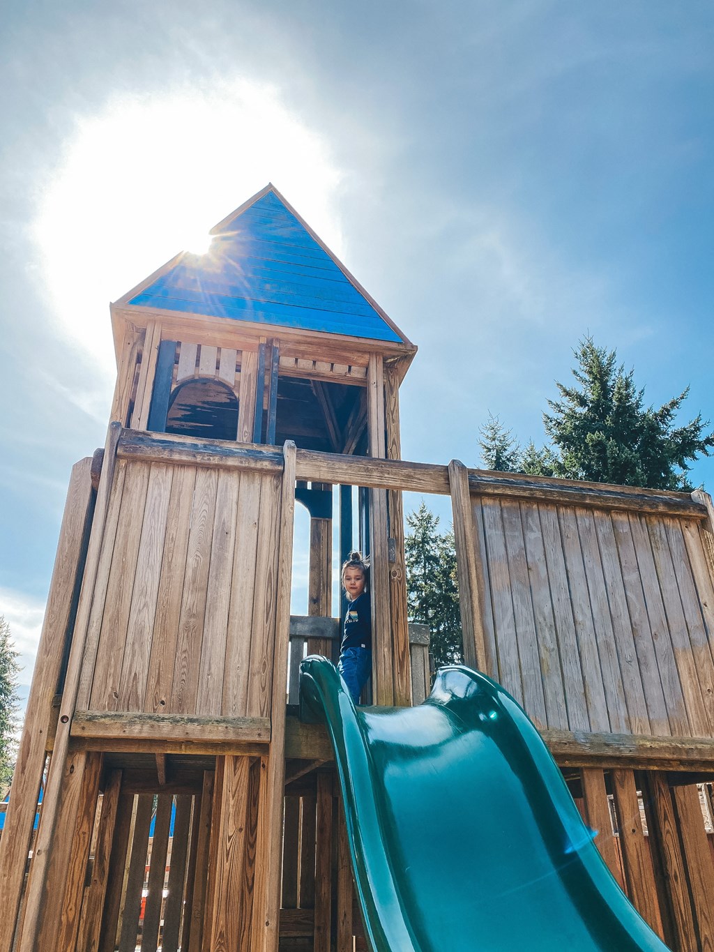 a young boy stands in the doorway of a wooden playset with a slide at Rivulet, Silverdale, 98383