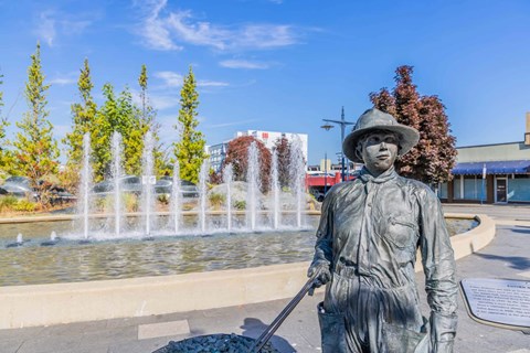 A statue of a person holding a shovel stands in front of a fountain  at Spyglass Hill Apartments, Bremerton, 98337