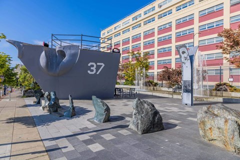 A large grey sculpture of a ship with the number 37 on it is in the foreground of a city square  at Spyglass Hill Apartments, Bremerton, 98337
