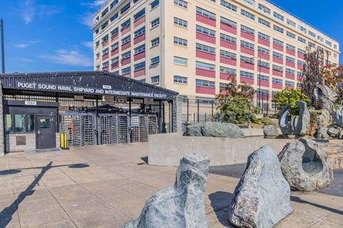 A large rock formation sits in front of a building with a sign that reads at Spyglass Hill Apartments, Bremerton, 98337