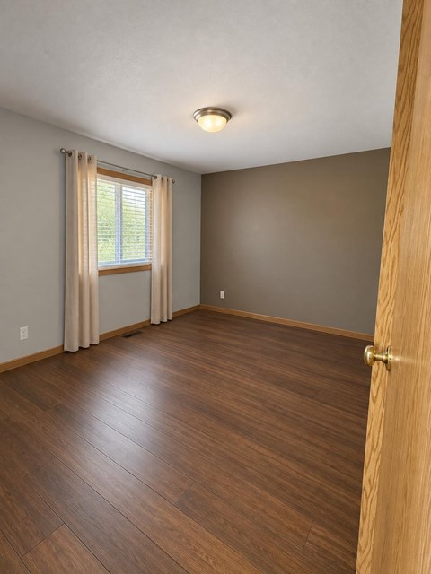 A room with a wooden floor and a window with curtains.