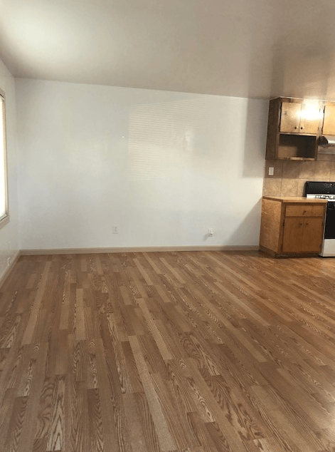 A room with wooden flooring and a kitchenette in the corner.