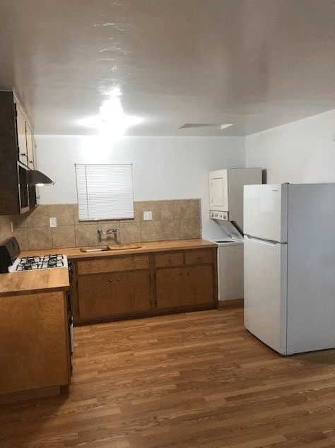 A kitchen with a white fridge and wooden floors.