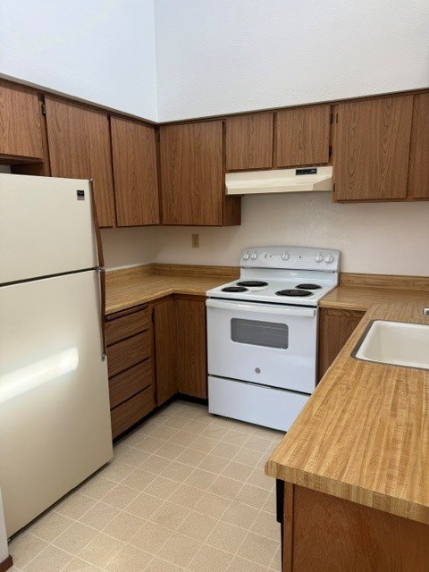 A kitchen with a white refrigerator, white stove, and wooden cabinets.