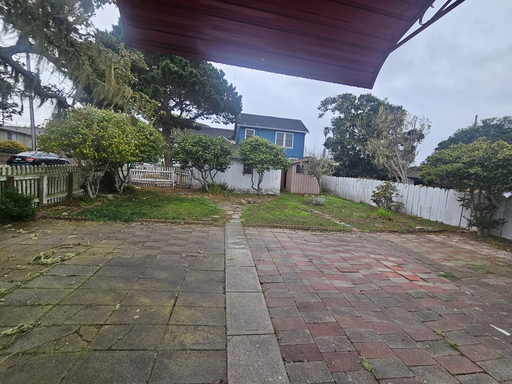the back yard of a house with a brick walkway and a blue house behind