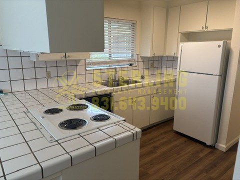 A kitchen with a white tiled stove top and a white fridge.