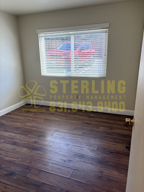 A Sterling Property Management sign is on a wall above a wooden floor in an empty room.