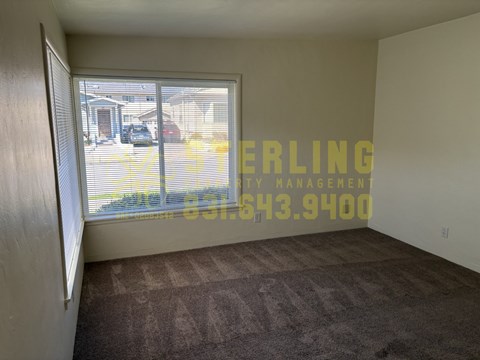 A room with a carpeted floor and a sliding glass door leading to a parking lot.