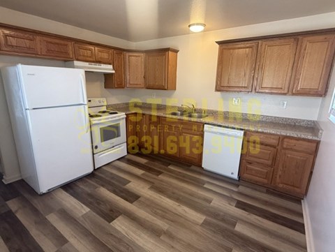 A kitchen with a white fridge, wooden cabinets, and a wooden floor.